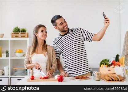 technology, people and eating concept - happy couple cooking food and taking selfie at home kitchen. couple cooking food and taking selfie at kitchen