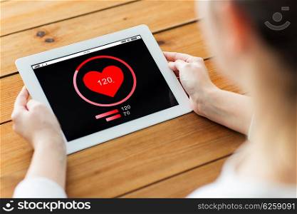 technology, people and health care concept - close up of woman with heart rate on tablet pc computer screen on wooden table