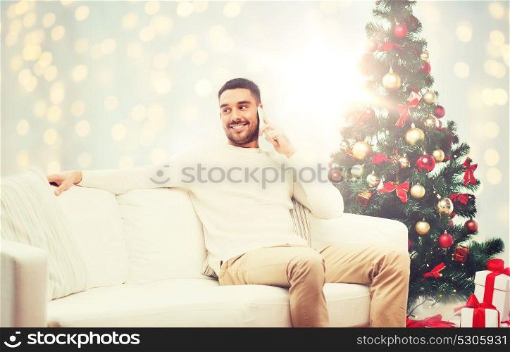 technology, people and holidays concept - smiling man calling on smartphone over christmas tree and lights background. man calling on smartphone for christmas