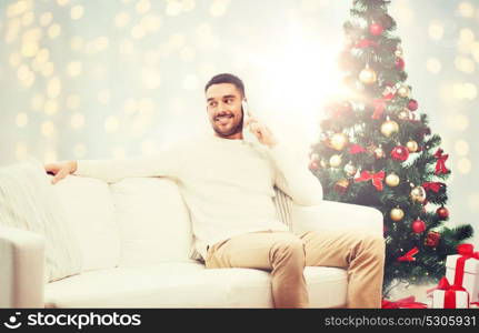 technology, people and holidays concept - smiling man calling on smartphone over christmas tree and lights background. man calling on smartphone for christmas