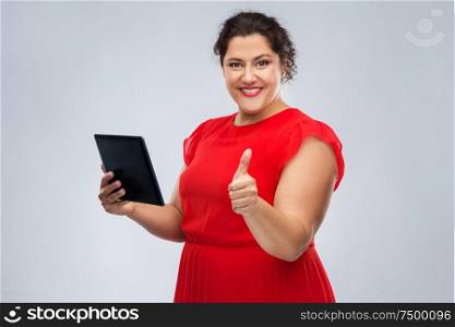 technology, people and internet concept - happy woman in red dress using tablet pc computer showing thumbs up over grey background. happy woman with tablet computer showing thumbs up