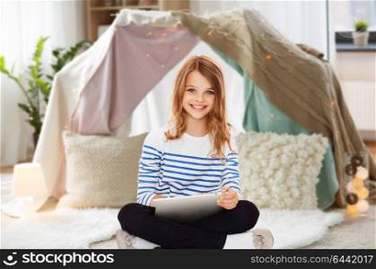 technology, people and internet concept - little student girl with tablet pc at home over kids room and tepee background. student girl with tablet pc at home