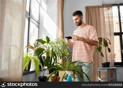 technology, people and internet concept - man with smartphone and flowers at home. man with smartphone and flowers at home