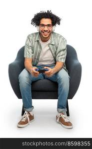 technology, people and leisure concept - happy smiling young man in headphones with gamepad sitting in chair and playing video game over white background. man in headphones with gamepad playing video game