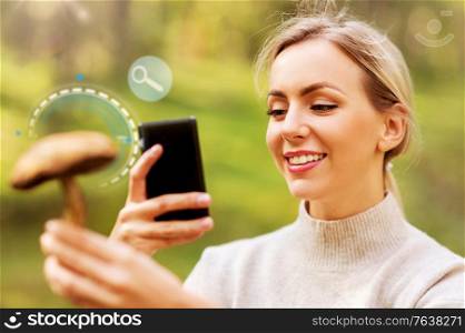 technology, people and leisure concept - happy smiling young woman with smartphone using search application to identify mushroom in forest. woman using smartphone to identify mushroom