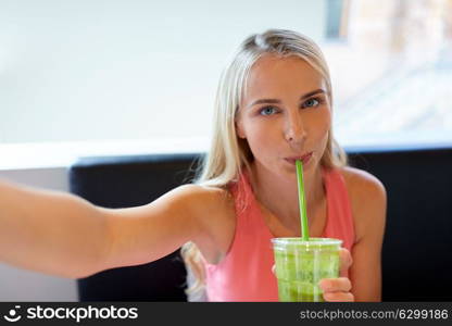 technology, people and leisure concept - happy woman drinking smoothie drink or vegetarian shake and taking selfie at restaurant. woman with smoothie taking selfie at restaurant