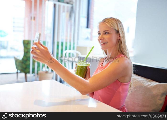 technology, people and leisure concept - happy woman with smartphone and smoothie drink or vegetarian shake taking selfie at restaurant. woman with smartphone taking selfie at restaurant