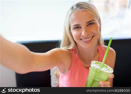 technology, people and leisure concept - happy woman with smoothie drink or vegetarian shake taking selfie at restaurant. woman with smoothie taking selfie at restaurant