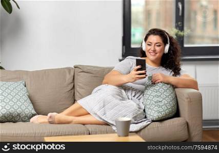 technology, people and leisure concept - happy young woman in headphones listening to music on smartphone at home. woman in headphones listens to music on smartphone