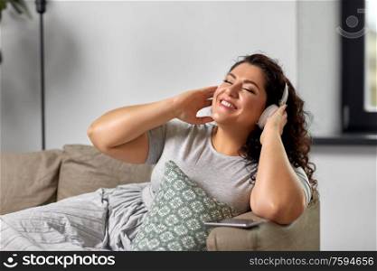 technology, people and leisure concept - happy young woman in headphones listening to music at home. woman in headphones listening to music at home