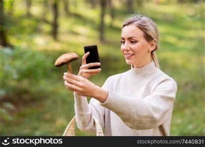 technology, people and leisure people concept - young woman with smartphone using app to identify mushroom in forest. woman using smartphone to identify mushroom