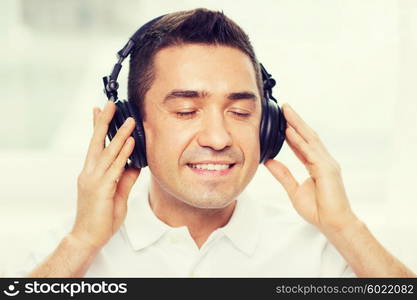 technology, people and lifestyle concept - happy man in headphones listening to music at home