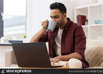 technology, people and lifestyle concept - happy man with laptop computer drinking coffee or tea at home. smiling man with laptop drinking coffee at home