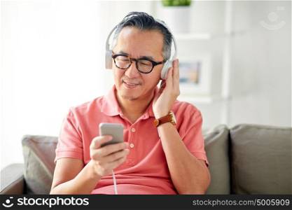 technology, people and lifestyle concept - happy man with smartphone and headphones listening to music at home. man with smartphone and headphones at home