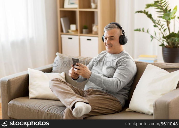 technology, people and lifestyle concept - happy man with smartphone and headphones listening to music at home. man with smartphone and headphones at home