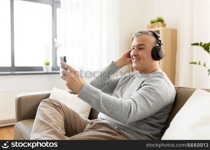 technology, people and lifestyle concept - happy man with smartphone and headphones listening to music at home. man with smartphone and headphones at home. man with smartphone and headphones at home