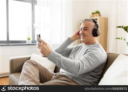 technology, people and lifestyle concept - happy man with smartphone and headphones listening to music at home. man with smartphone and headphones at home. man with smartphone and headphones at home