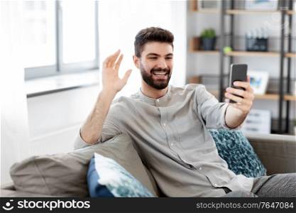 technology, people and lifestyle concept - happy man with smartphone having video call at home. man with smartphone having video call at home