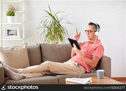 technology, people and lifestyle concept - happy man with tablet pc computer and headphones listening to music at home. man with tablet pc and headphones at home