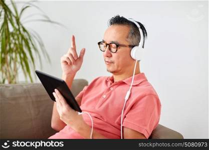 technology, people and lifestyle concept - happy man with tablet pc computer and headphones listening to music at home. man with tablet pc and headphones at home