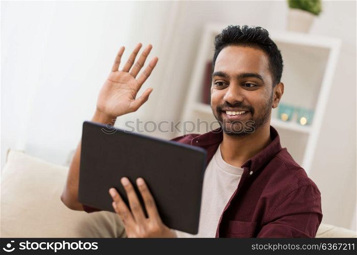 technology, people and lifestyle concept - happy man with tablet pc computer having video chat at home and waving hand. happy man with tablet pc having video chat at home