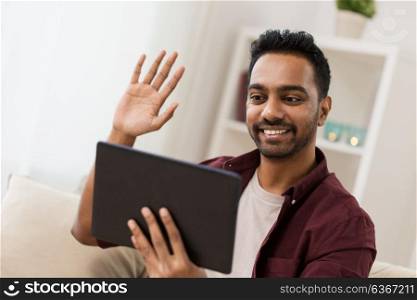 technology, people and lifestyle concept - happy man with tablet pc computer having video chat at home and waving hand. happy man with tablet pc having video chat at home