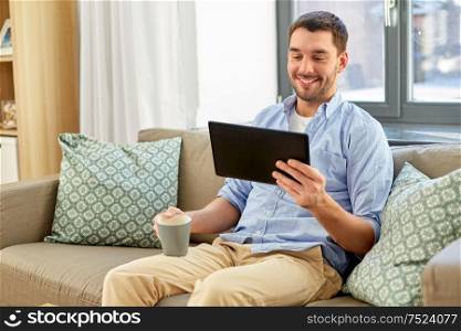 technology, people and lifestyle concept - happy man with tablet pc computer drinking coffee or tea at home. smiling man with tablet pc drinking coffee at home