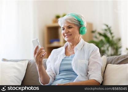 technology, people and lifestyle concept - happy senior woman in headphones and smartphone listening to music at home. senior woman in headphones listening to music