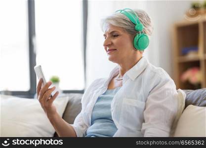 technology, people and lifestyle concept - happy senior woman in headphones and smartphone listening to music at home. senior woman in headphones listening to music