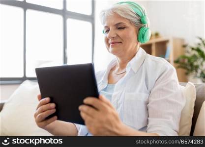technology, people and lifestyle concept - happy senior woman in headphones and tablet pc computer listening to music at home. senior woman in headphones listening to music