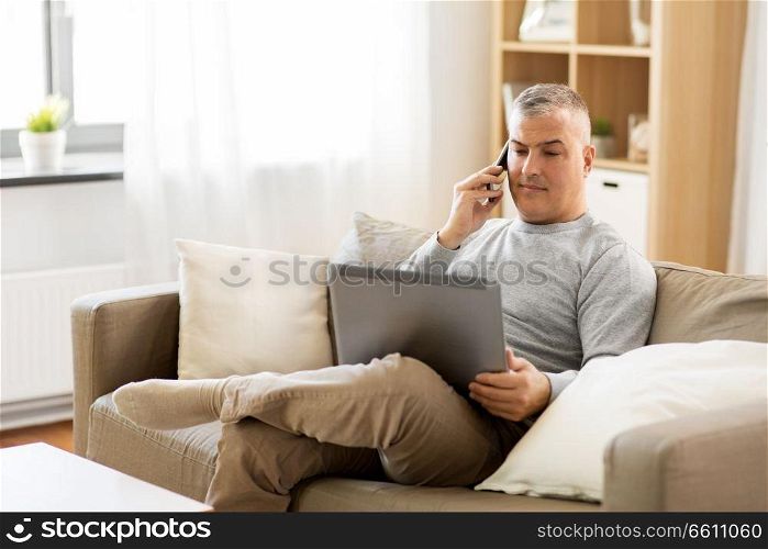 technology, people and lifestyle concept - man with laptop computer sitting on sofa at home and calling on smartphone. man with laptop calling on smartphone at home