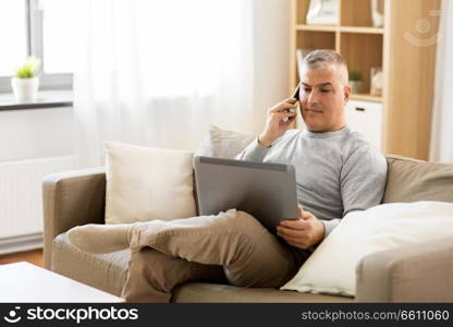 technology, people and lifestyle concept - man with laptop computer sitting on sofa at home and calling on smartphone. man with laptop calling on smartphone at home