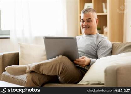 technology, people and lifestyle concept - man with laptop computer sitting on sofa at home. man with laptop computer sitting on sofa at home
