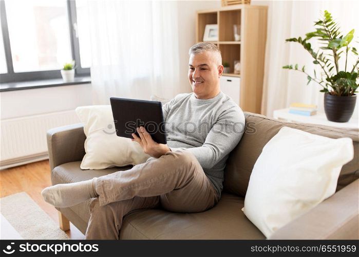 technology, people and lifestyle concept - man with tablet pc computer sitting on sofa at home. man with tablet pc sitting on sofa at home. man with tablet pc sitting on sofa at home