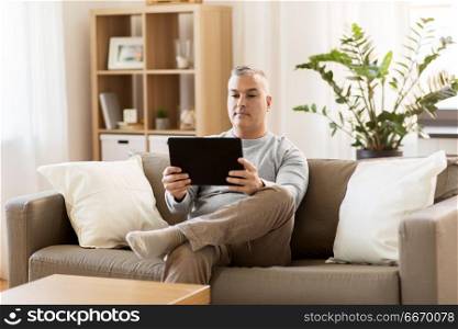 technology, people and lifestyle concept - man with tablet pc computer sitting on sofa at home. man with tablet pc sitting on sofa at home. man with tablet pc sitting on sofa at home