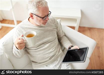 technology, people and lifestyle concept - senior man with tablet pc computer drinking tea at home