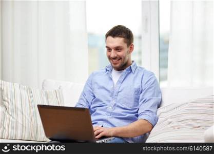 technology, people and lifestyle concept - smiling man working with laptop at home