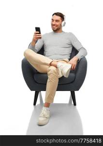 technology, people and music concept - happy smiling man with smartphone and earphones sitting in chair over white background. man with phone and headphones sitting in chair
