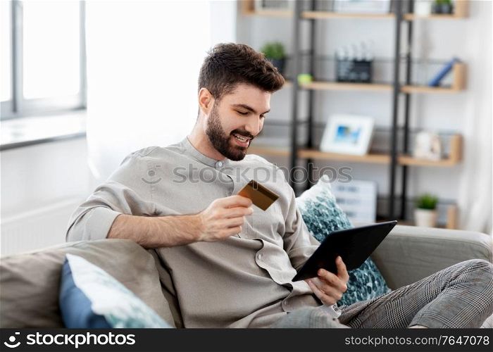 technology, people and online shopping concept - happy smiling man with tablet pc computer and credit card at home. man with tablet computer and credit card at home