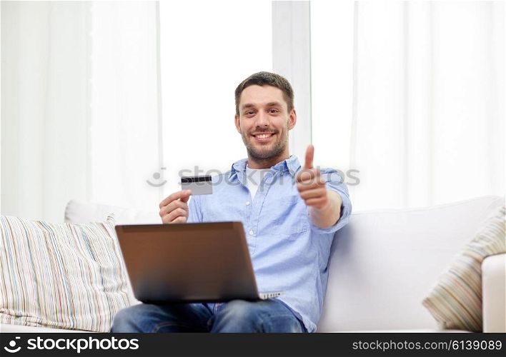 technology, people and online shopping concept - smiling man with laptop and credit card at home showing thumbs up