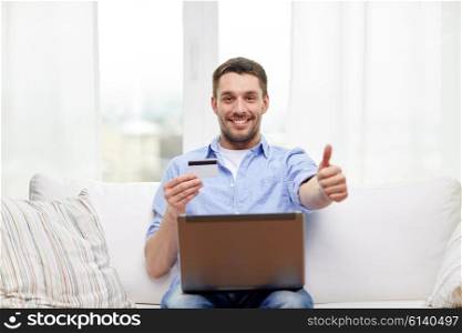 technology, people and online shopping concept - smiling man with laptop and credit card at home showing thumbs up