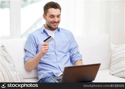 technology, people and online shopping concept - smiling man with laptop and credit card at home