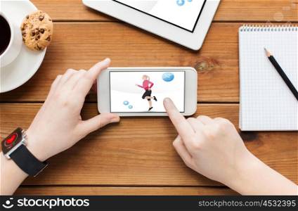 technology, people and sport concept - close up of woman with fitness application on smartphone screen and coffee cup on wooden table