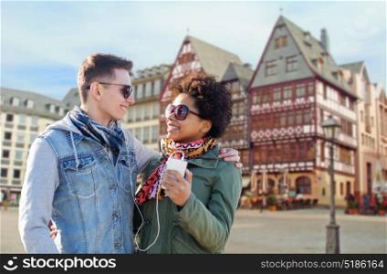 technology, people and travel concept - smiling couple with smartphone and earphones listening to music over frankfurt am main city street background. couple with smartphone and earphones in frankfurt