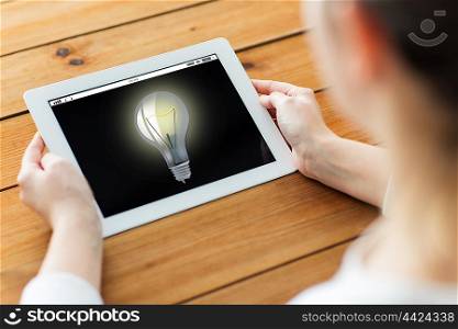 technology, people, business, idea and startup concept - close up of woman with light bulb on tablet pc computer screen on wooden table