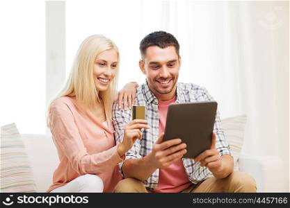 technology, people, e-money and commerce concept - smiling happy couple with tablet pc computer and credit or bank card shopping online at home