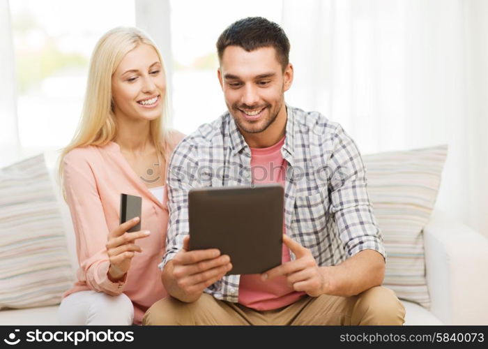 technology, people, e-money and commerce concept - smiling happy couple with tablet pc computer and credit or bank card shopping online at home