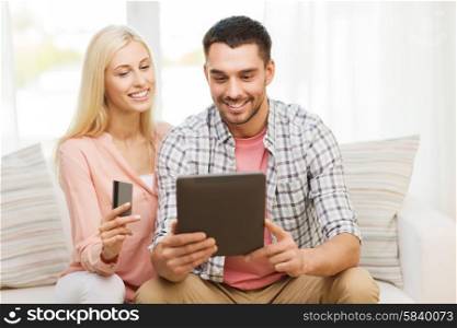technology, people, e-money and commerce concept - smiling happy couple with tablet pc computer and credit or bank card shopping online at home