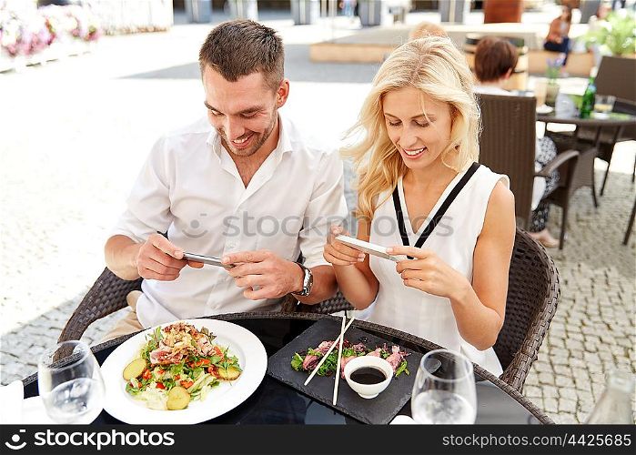 technology, people, eating and leisure concept - happy couple with smatphone taking picture of food at restaurant terrace