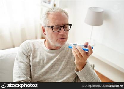 technology, people, lifestyle and communication concept - close up of senior man using voice command recorder or calling on smartphone at home